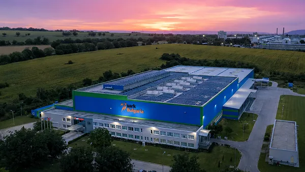 Blue industrial building with a red ribbon logo, illuminated at sunset with solar panels on the roof.