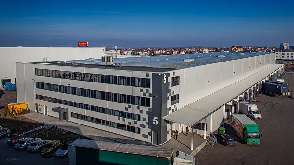 White multi-story industrial building marked with a large number 5, with loading docks and a city skyline behind.