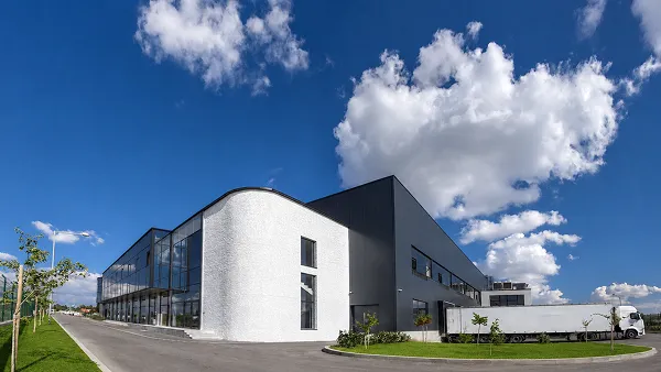 Modern industrial building with a curved white and dark facade and a truck parked outside.