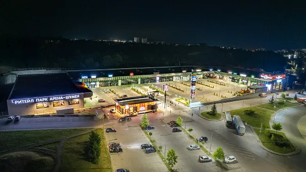 Aerial night view of a retail park with illuminated storefronts and a parking lot.