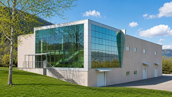 Modern office building with a green-tinted glass facade set against a hillside.