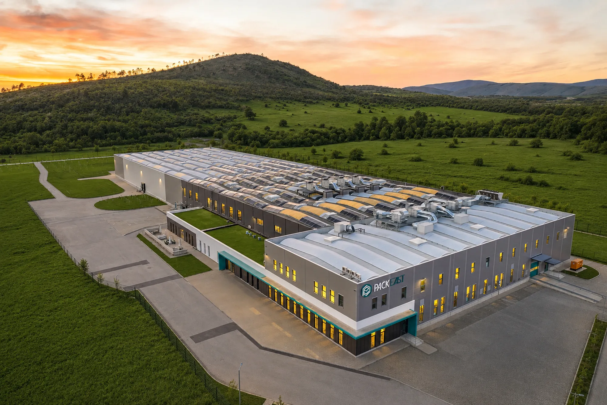 Industrial facility at sunset, with a colorful building illuminated against green hills.