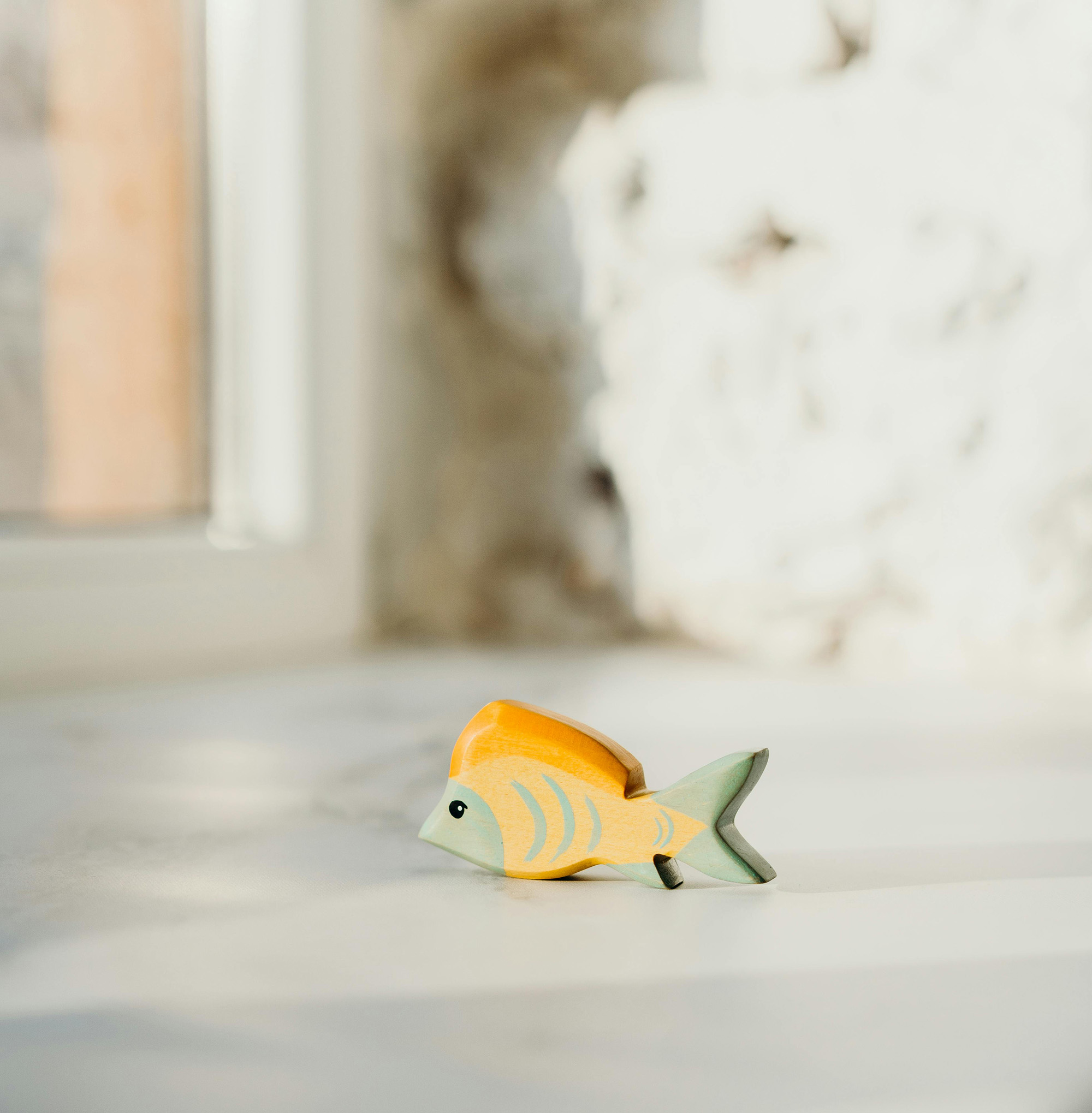 Small yellow and green wooden fish toy on a light surface with a blurred background.