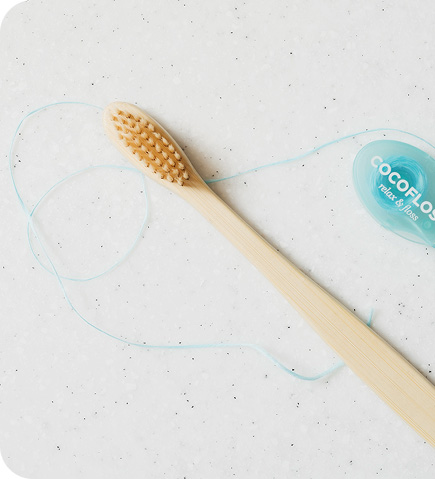 Wooden toothbrush with beige bristles and blue dental floss on a white speckled surface.