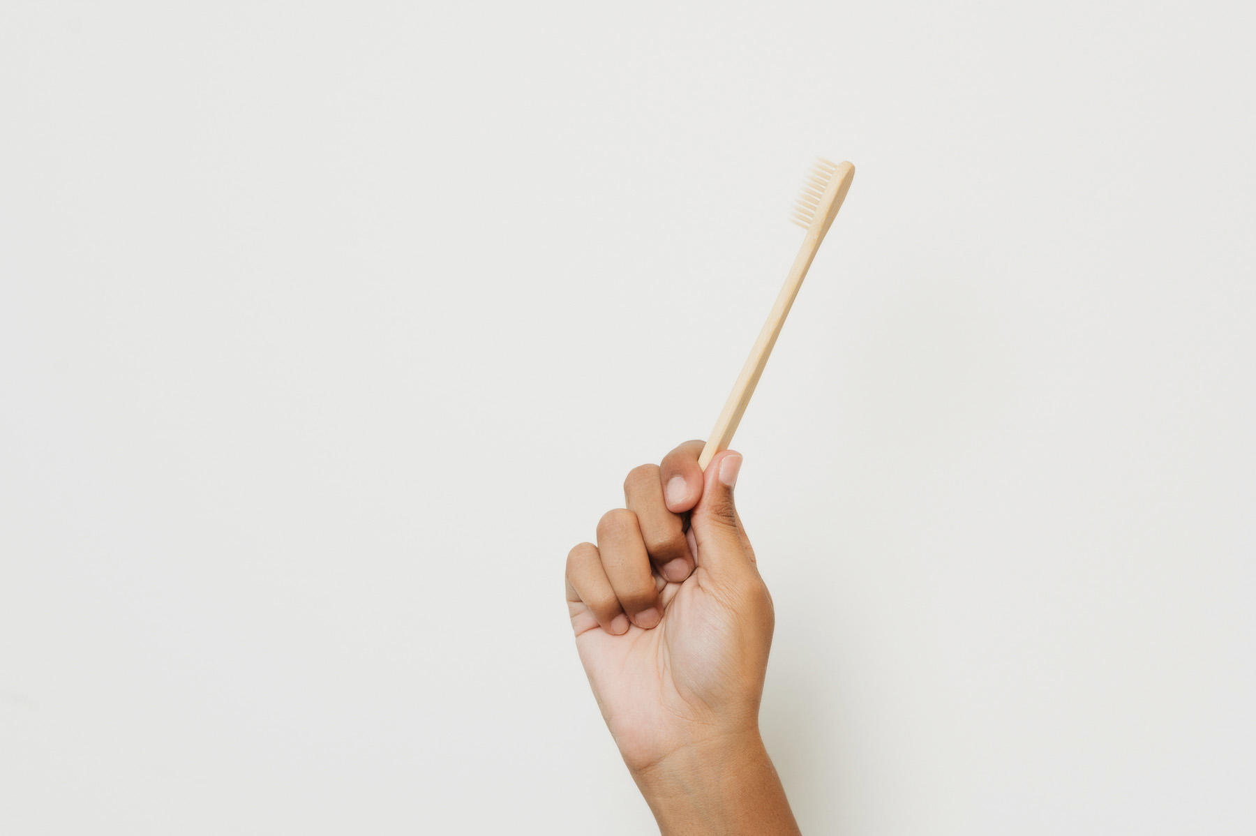 Hand holding a bamboo toothbrush against a plain white background.