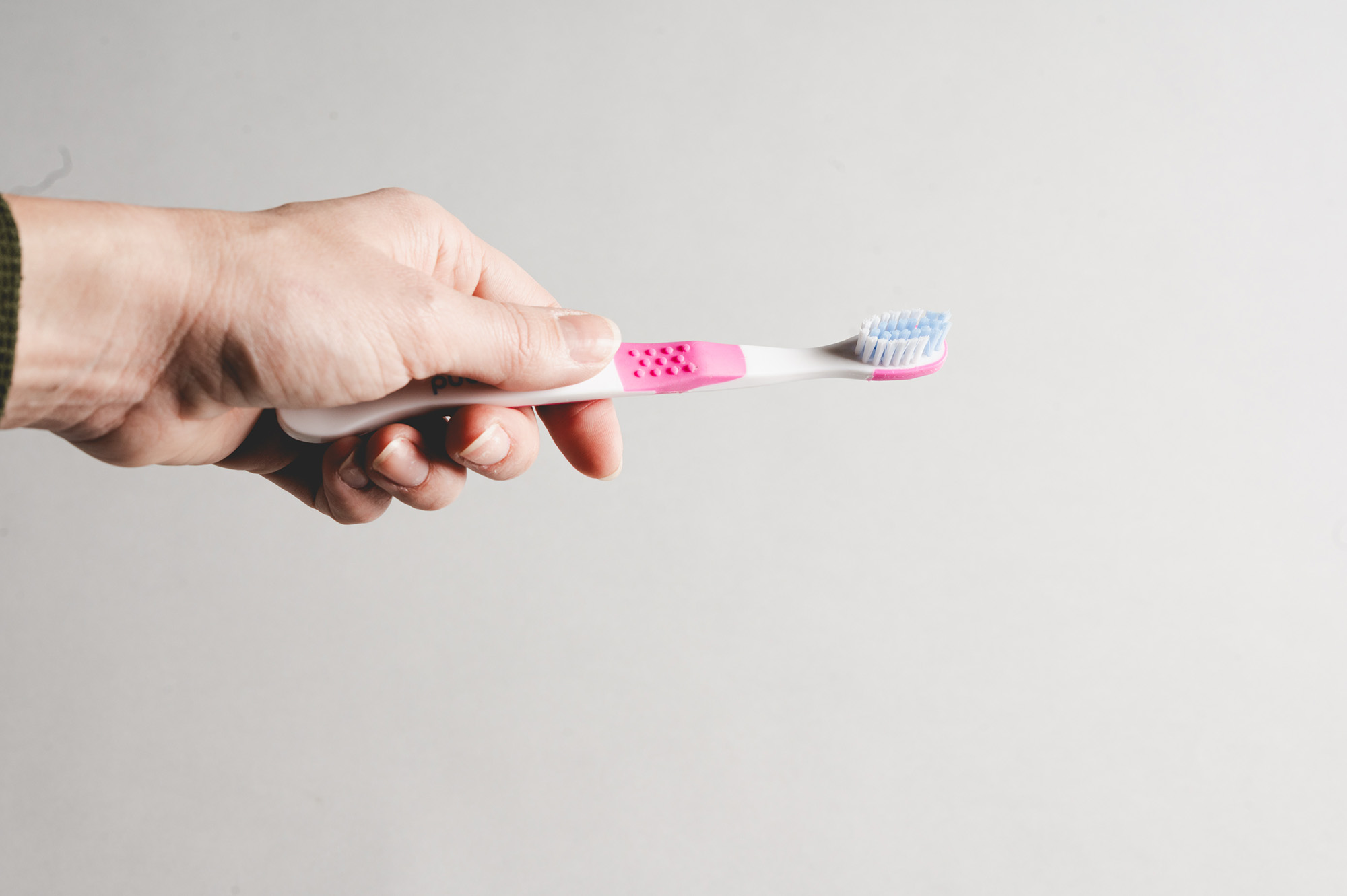Hand holding a white toothbrush with pink accents and blue bristles against a plain background.