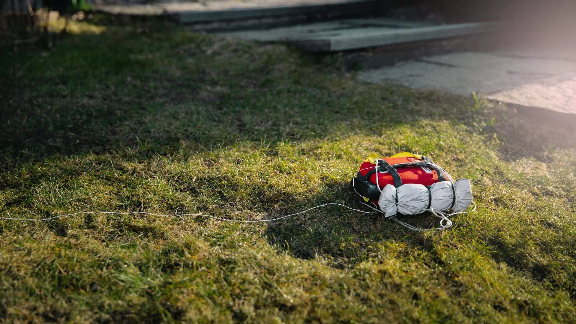 An AED lowered by the Everdrone aircraft lies on the grass, still attached to the winch line