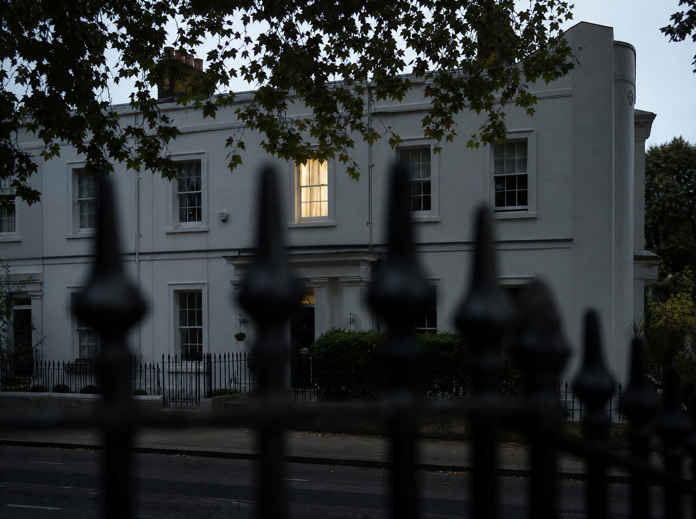 A white stuccoed terrace at dusk seen past dark iron railings