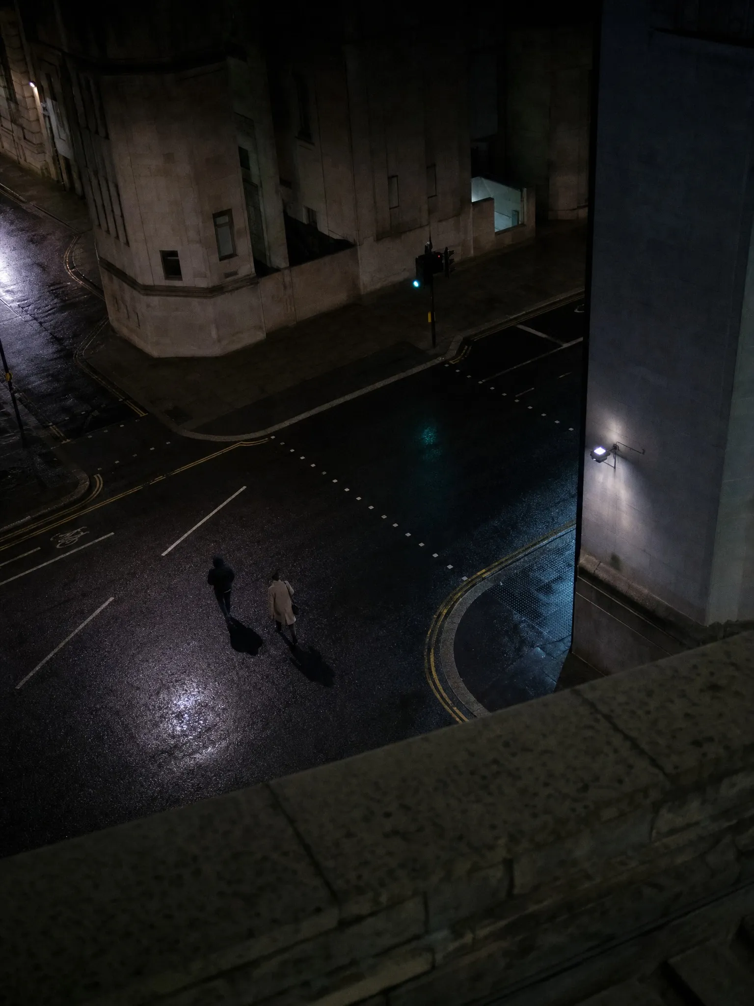 A wet street junction seen from above at night, a lone pedestrian crossing
