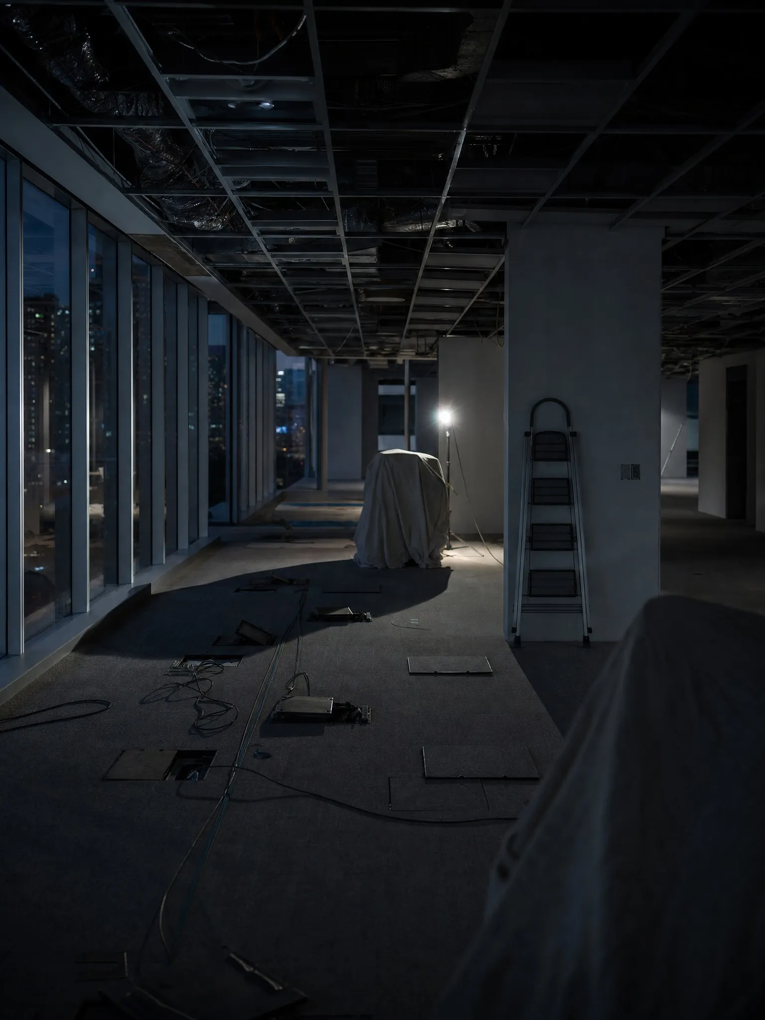An office floor under refurbishment with the ceiling opened and dust sheets over the furniture