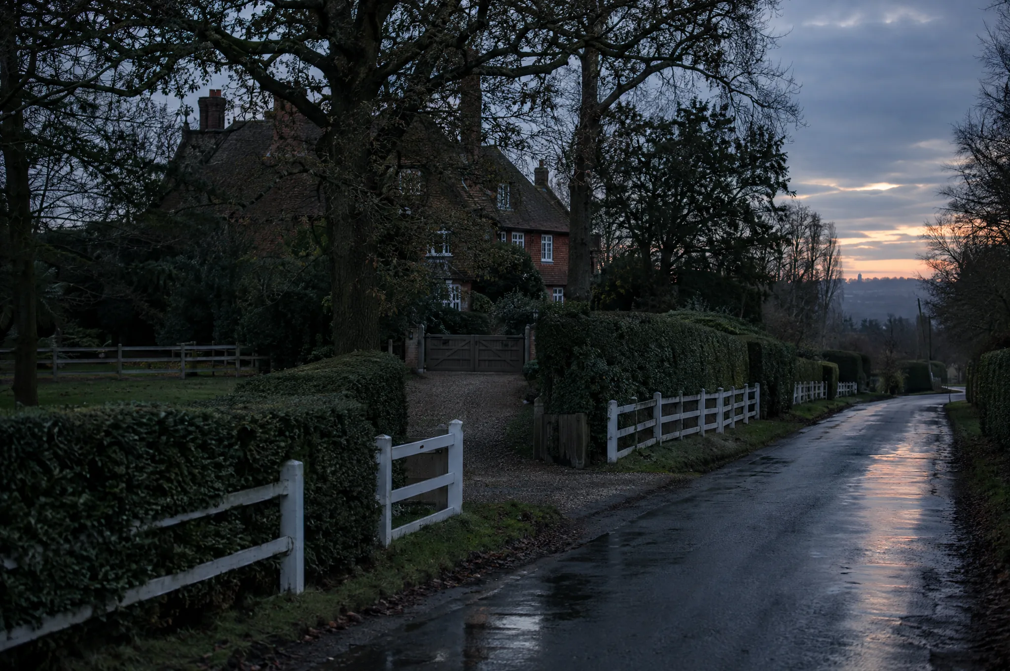A hedged Totteridge lane past white post and rail fencing and a gated drive at dusk