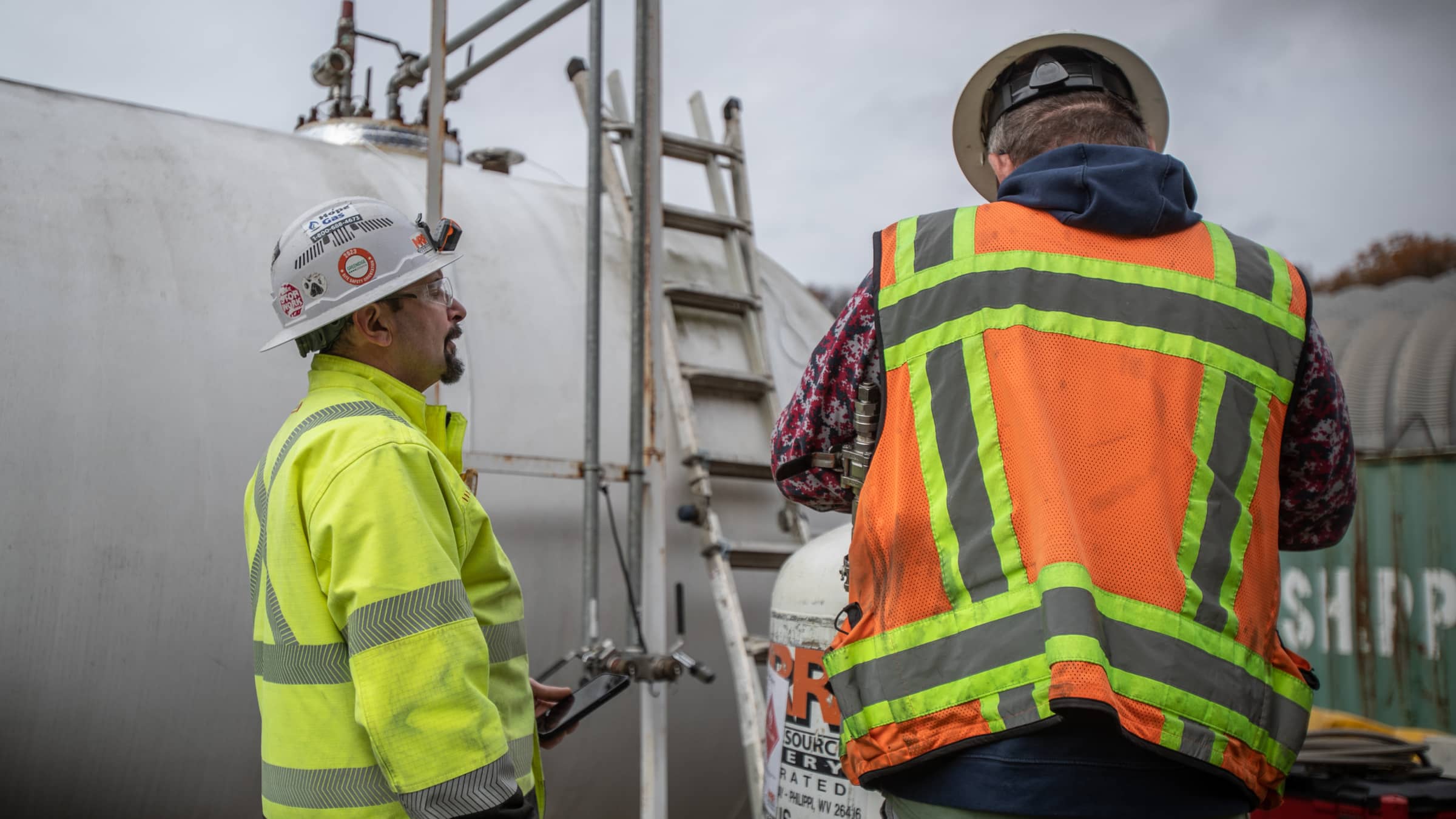 Two men wearing safety equipment talking near tank