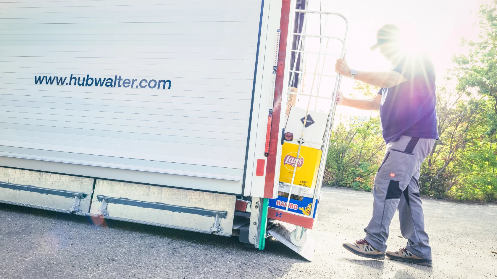 Mitarbeiter entlädt Warenwagen aus einem Hubwalter Kofferaufbau vor einem Personaleingang.