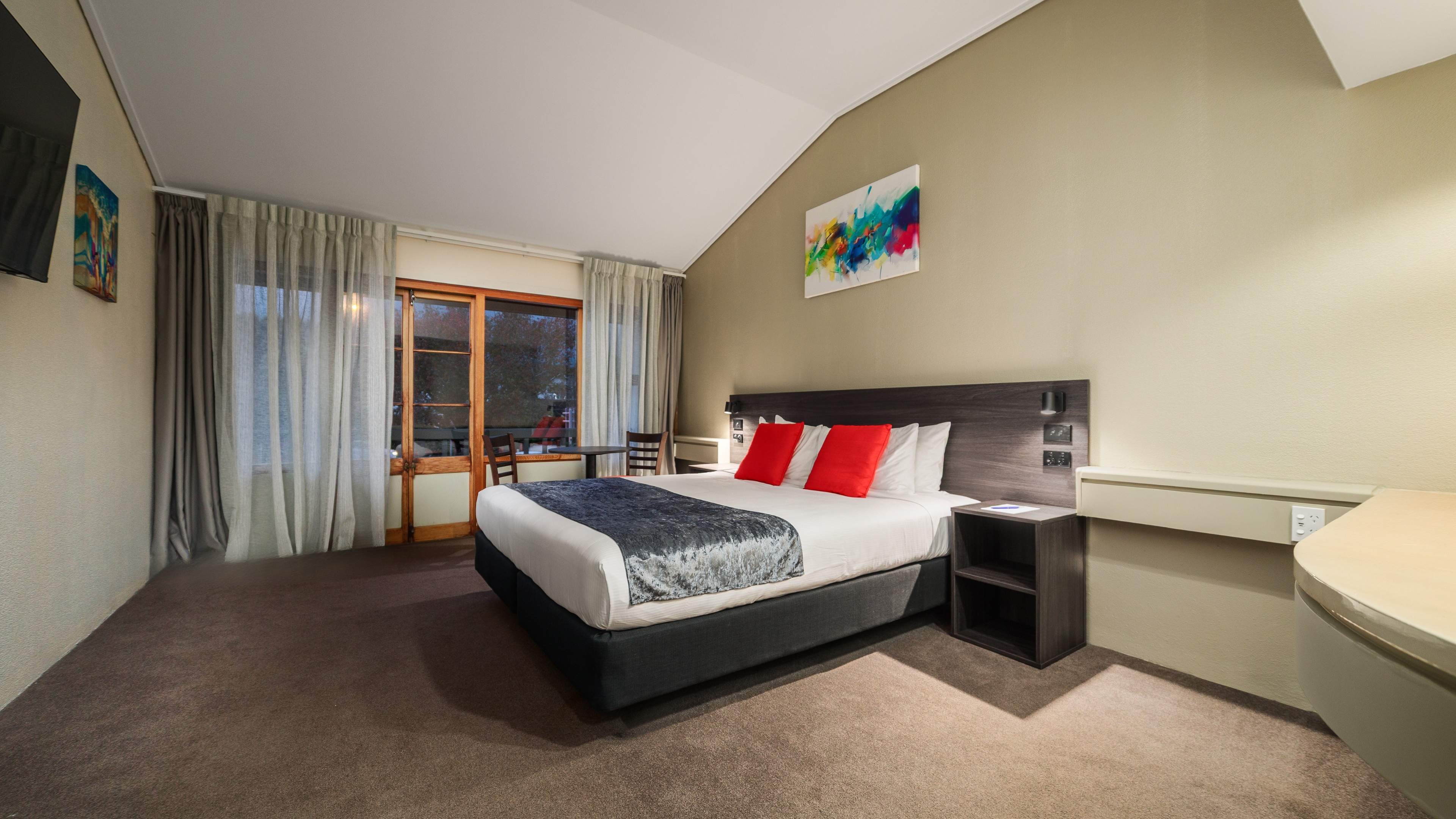 Modern hotel room with two single beds, blue geometric wall art, large window with city view, and a desk with flowers.