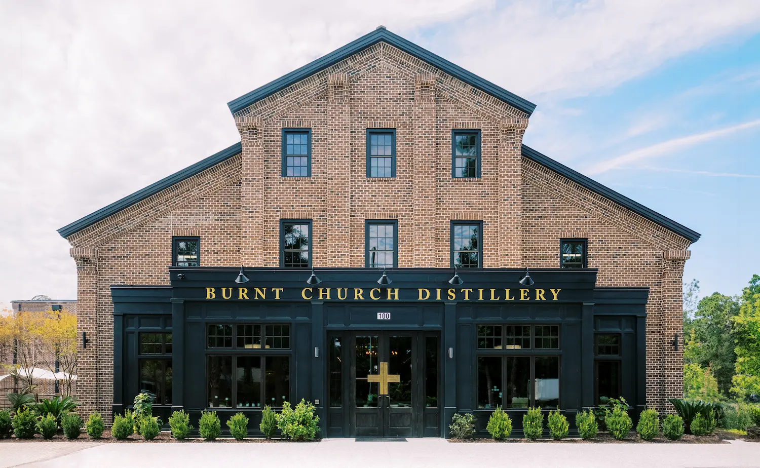 Brick building facade of Burnt Church Distillery with black trim and gold lettering above entrance.