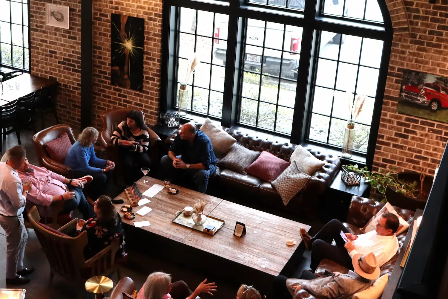 Guests seated on leather sofas and armchairs in a VIP lounge at Burnt Church Distillery, with exposed brick and tall arched windows.