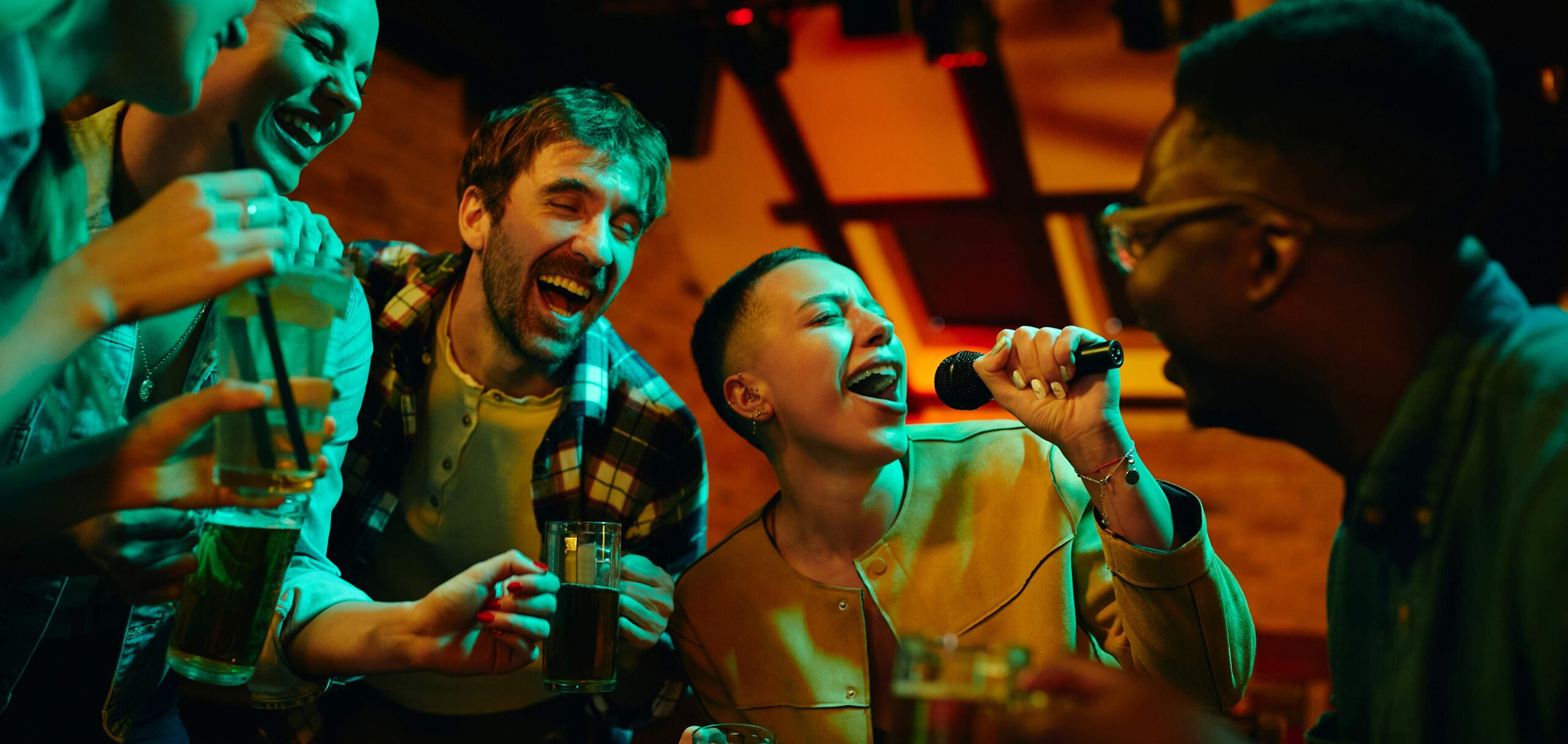 Group of friends enjoying karaoke night with drinks as one person sings into a microphone.