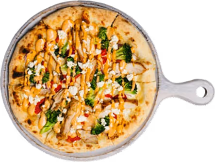 Pizza with broccoli, grilled chicken, cheese, and drizzled sauce on a wooden serving board.