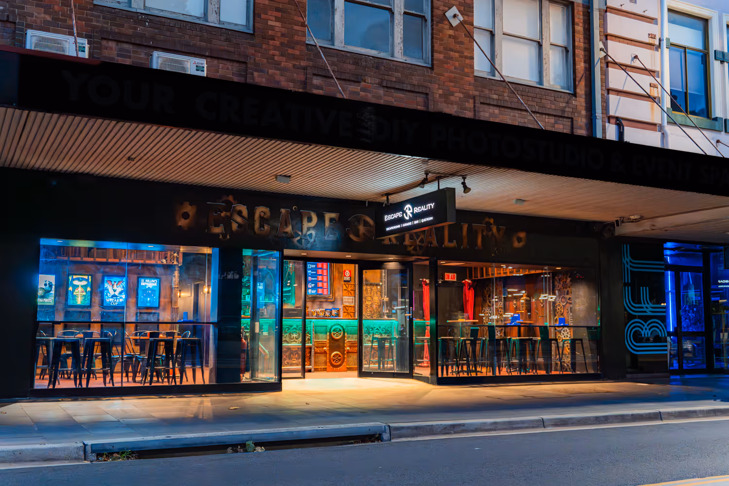 Night view of a modern escape room and bar with colorful neon lights and tall stools.