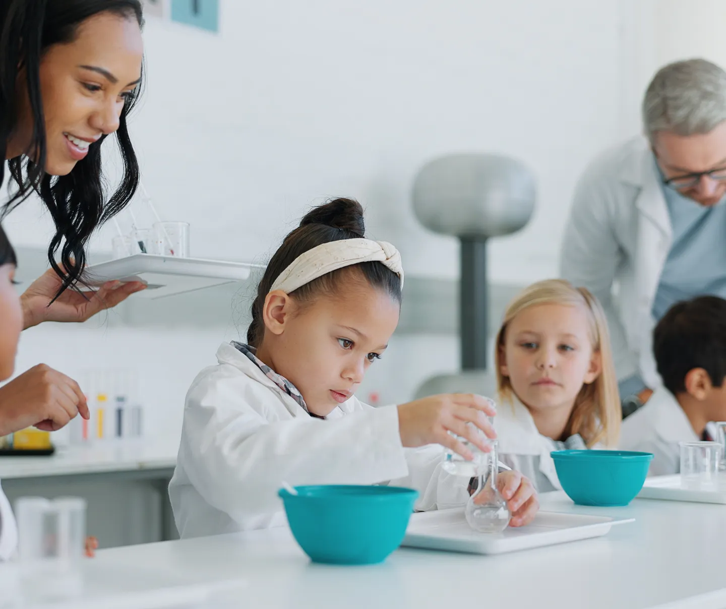 Young students in lab coats conducting science experiments with teacher assistance in a bright classroom.