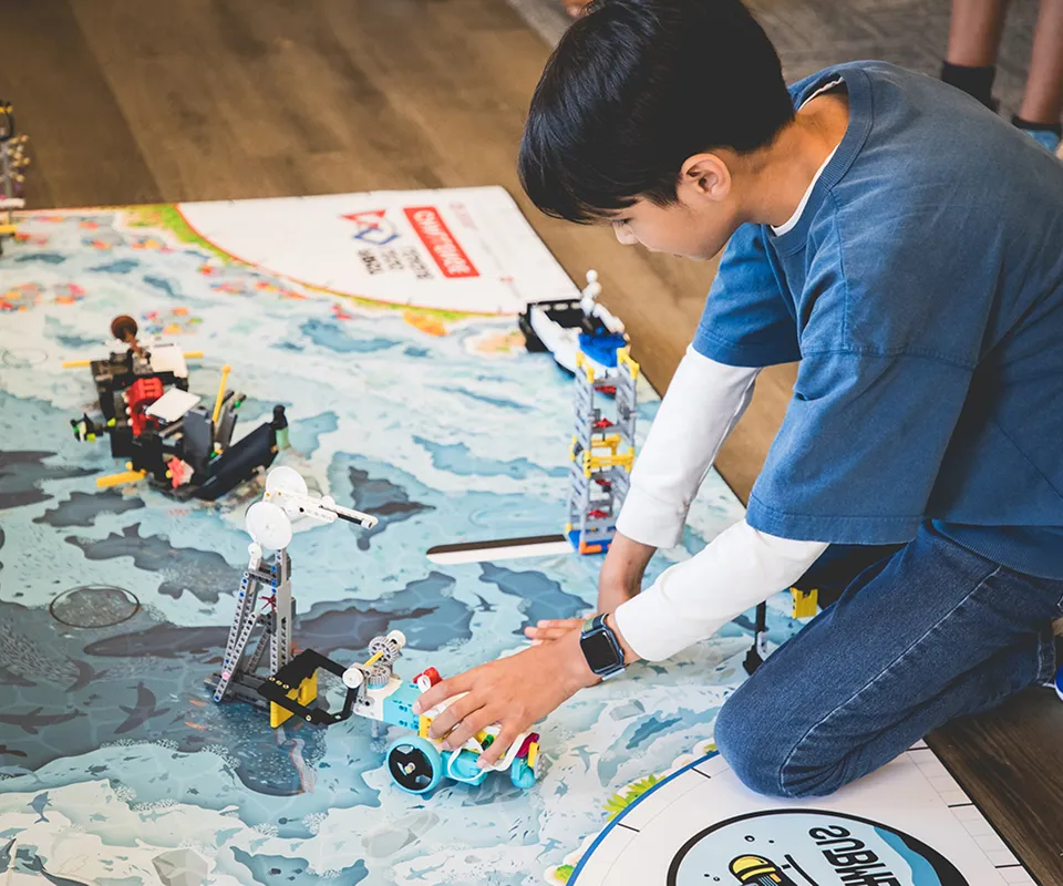 Boy kneeling on floor playing with robotic toys on a map-themed playmat indoors.