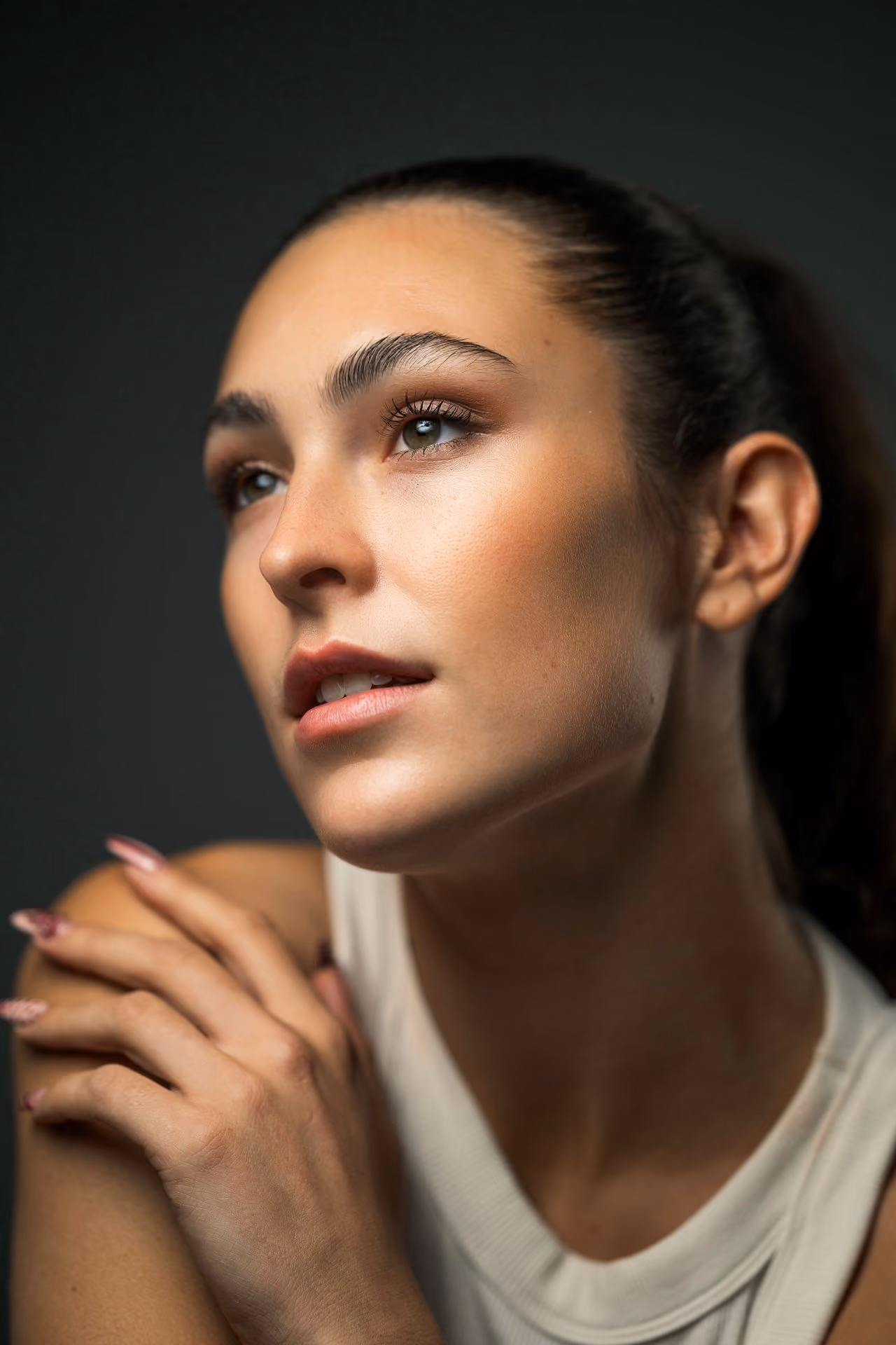 Close-up portrait of a Yaman Kelemet with smooth skin and natural makeup looking thoughtfully to the side against a dark background.