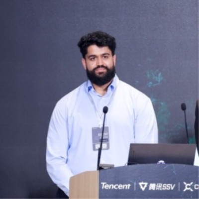Trishan Sharma behind a podium with a laptop, speaking at an event.