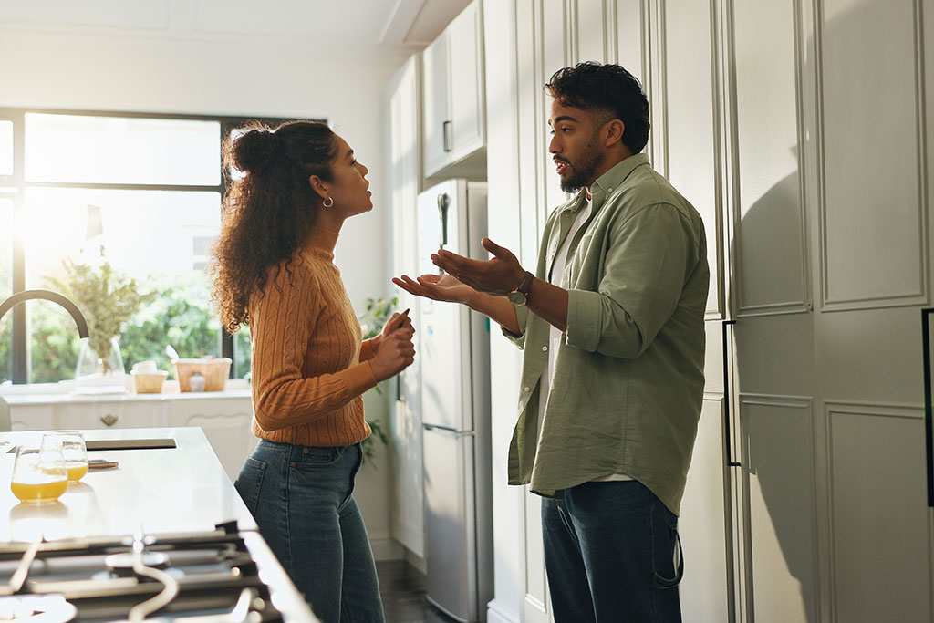 A man and woman having a tense discussion or argument while standing in a bright kitchen.