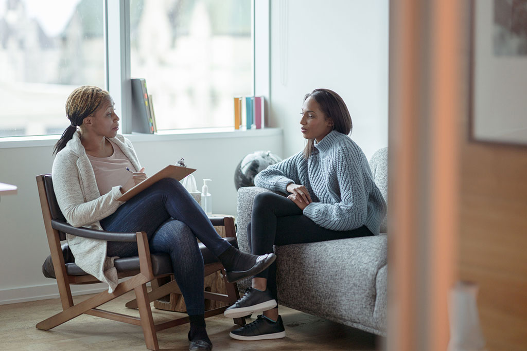 A therapist taking notes on a clipboard while listening to a client during a counselling session.
