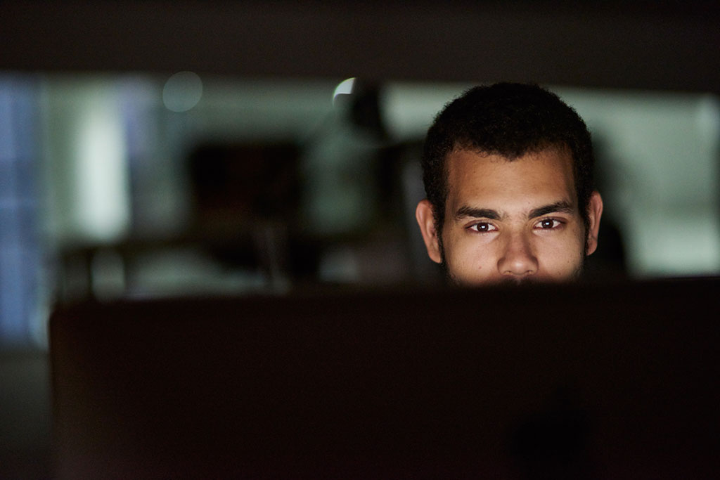 A man looking intently at a computer screen in a dimly lit office environment.