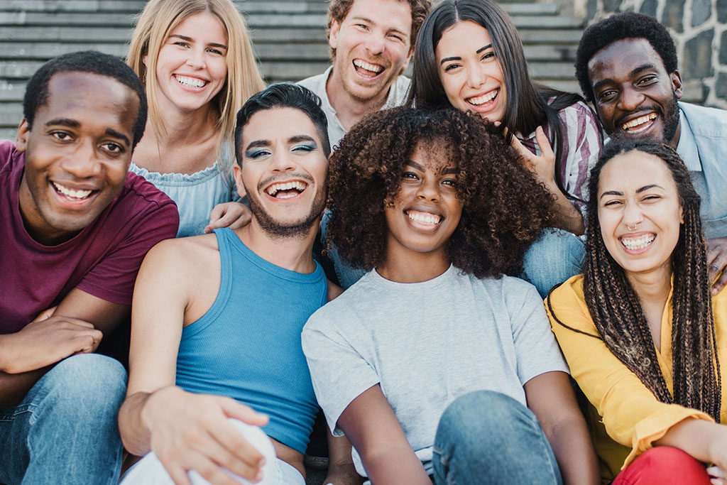 A diverse group of young adults laughing and smiling together while sitting outdoors on stone steps.