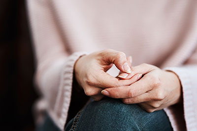 A close-up of a person nervously picking at their fingernails and wringing their hands in their lap, conveying anxiety or stress.