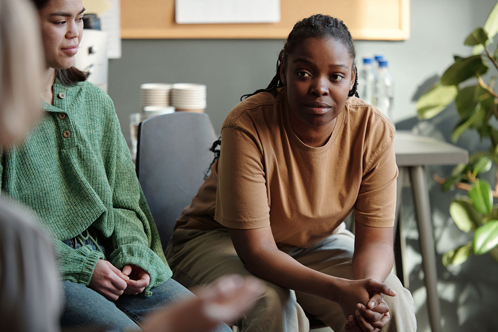 A Black woman with braids listening intently during a group therapy session or community support circle.