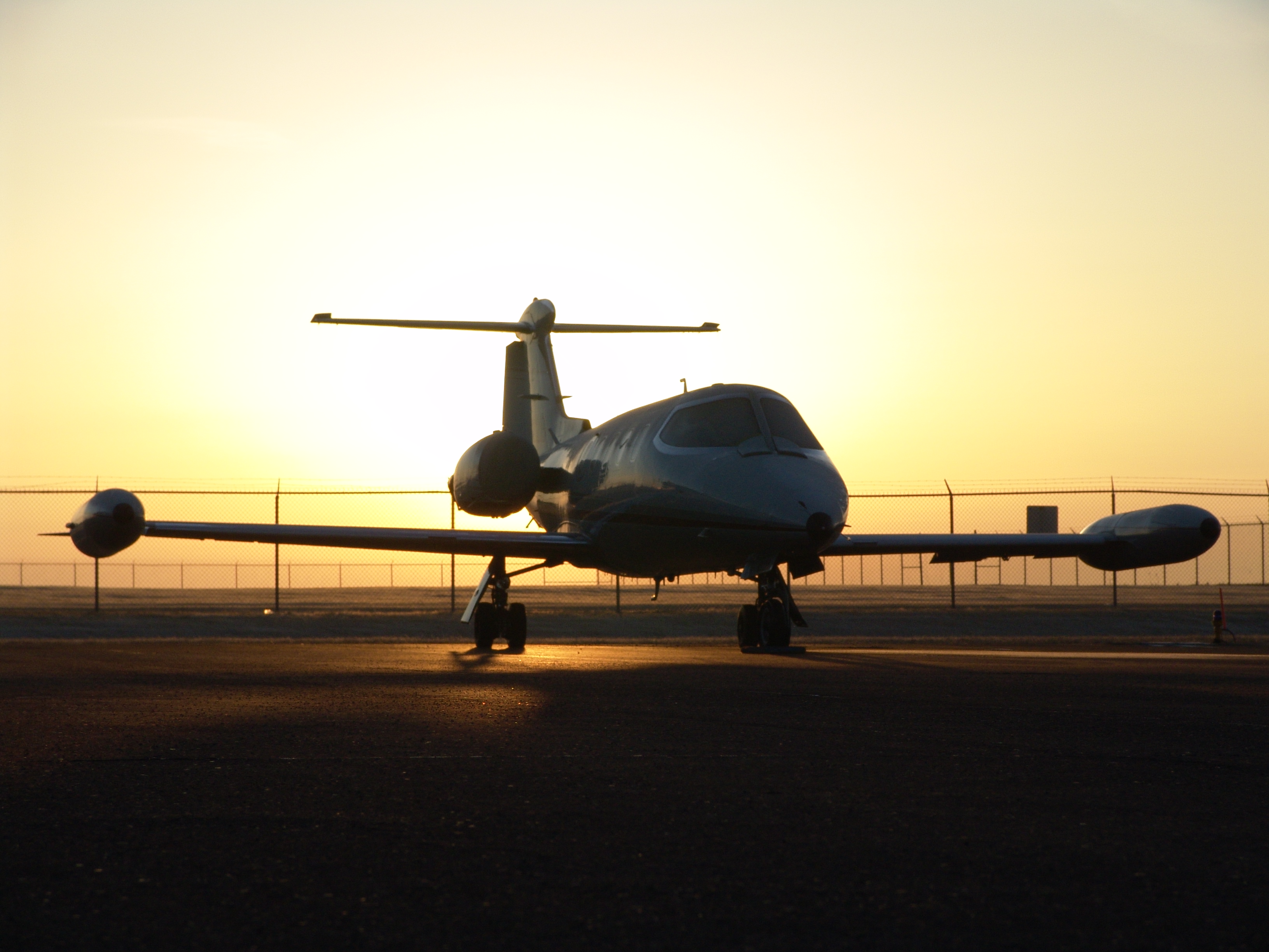 A small private jet parked on an airport tarmac, silhouetted against a golden sunset.