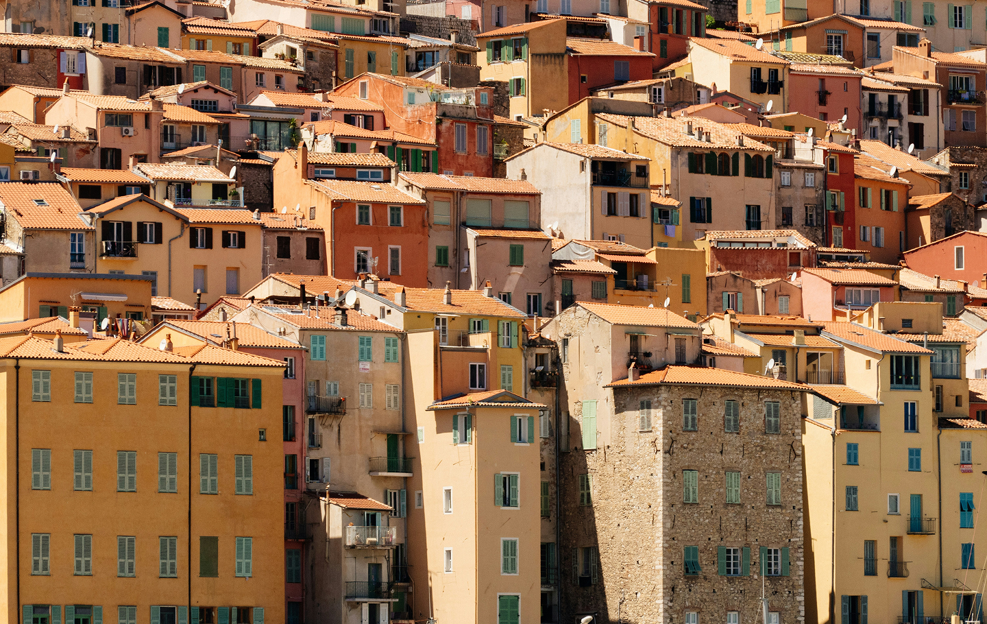 Cluster of pastel-colored Mediterranean houses with terracotta roofs tightly packed on a hillside.