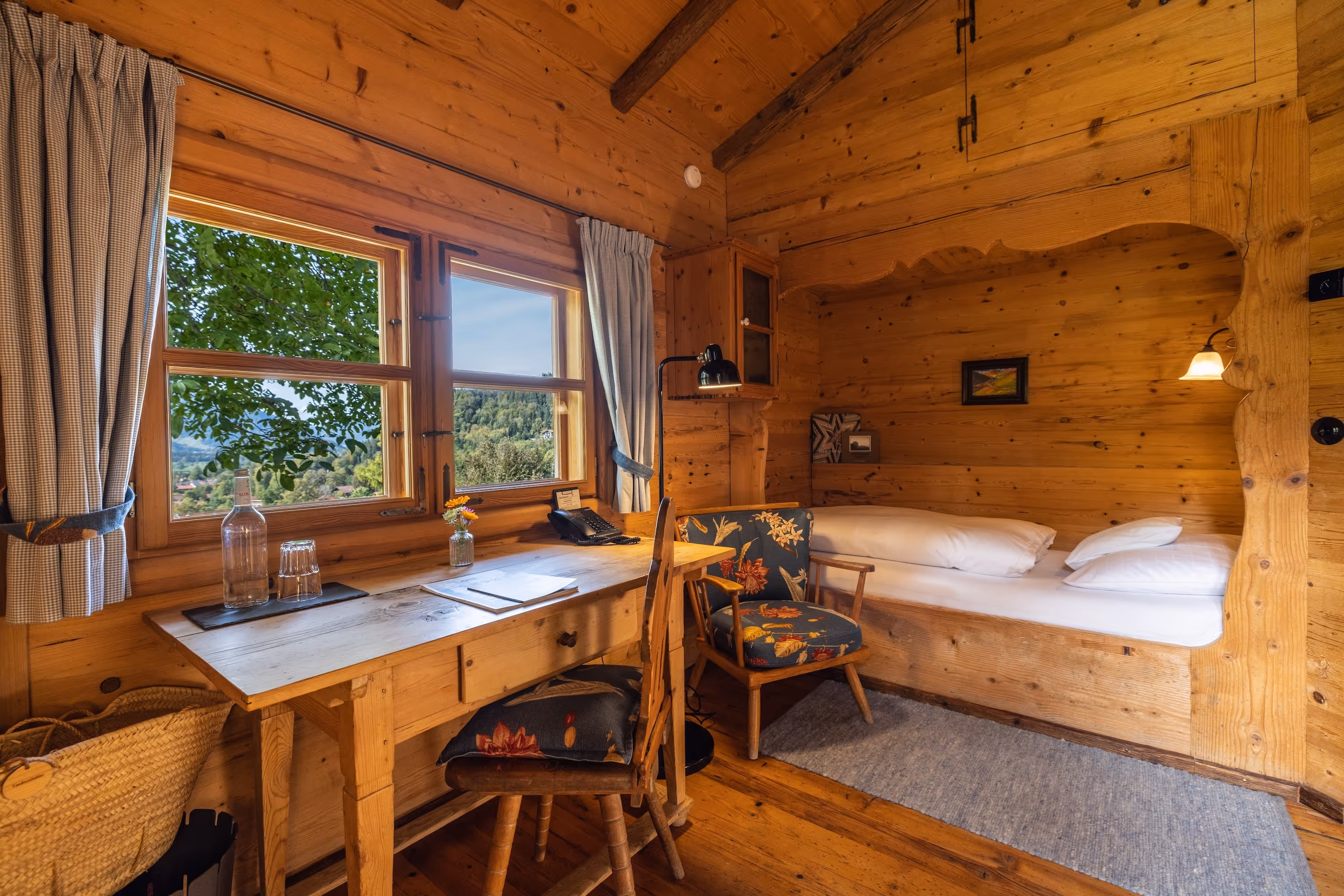 Bettnische mit Bauernstuhl in einer Lufthütte des Naturhotels Tannerhof – Sinnbild für den rustikalen Rückzug am Hang bei Bayrischzell.
