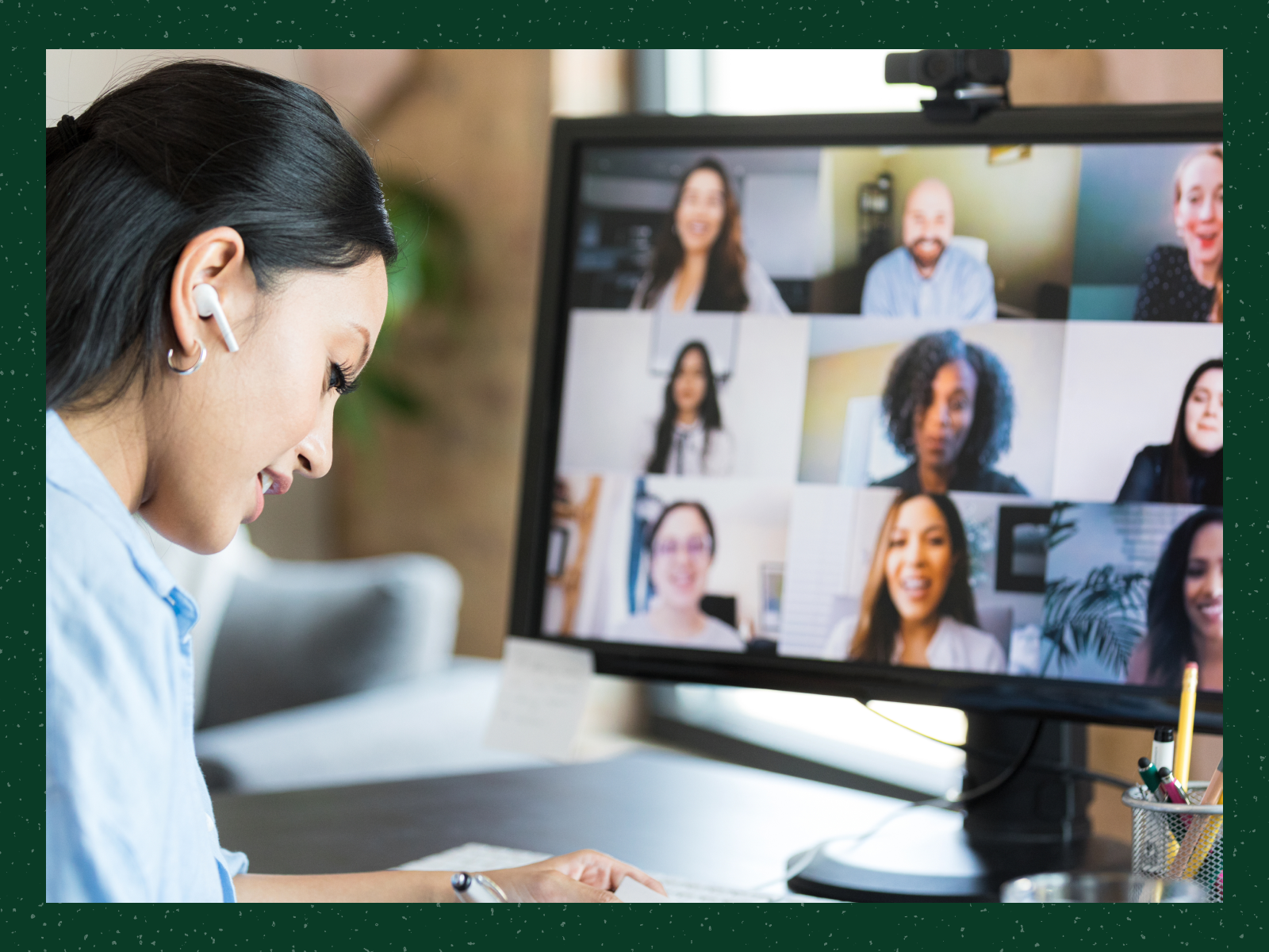 Woman wearing earbuds writing notes while attending a video conference with eight people on screen.