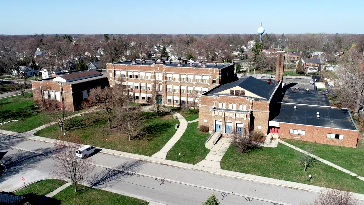 Aerial view of the all-brick school building with multiple sections and a water tower in the background.