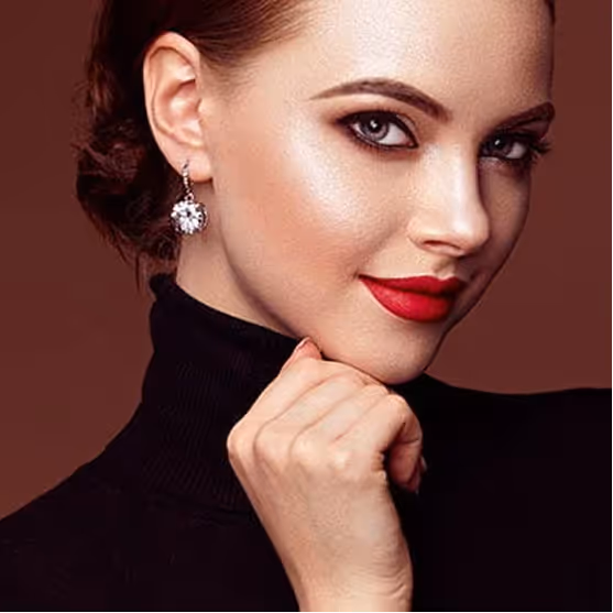 Close-up of a woman with red lipstick, smoky eye makeup, and a black turtleneck against a brown background.