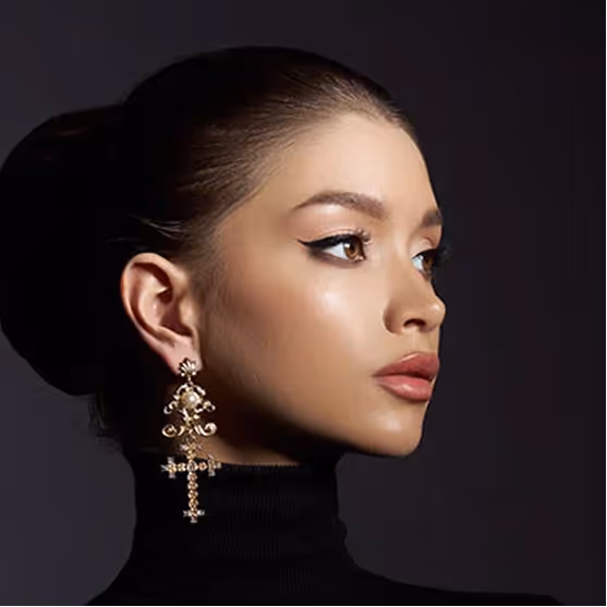 Profile of a woman with slicked-back hair, winged eyeliner, bold earrings, and nude lipstick.