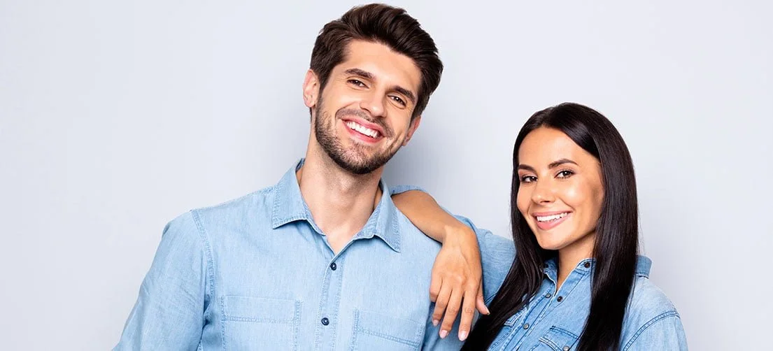 Smiling man and woman in denim shirts posing together against a plain light background.