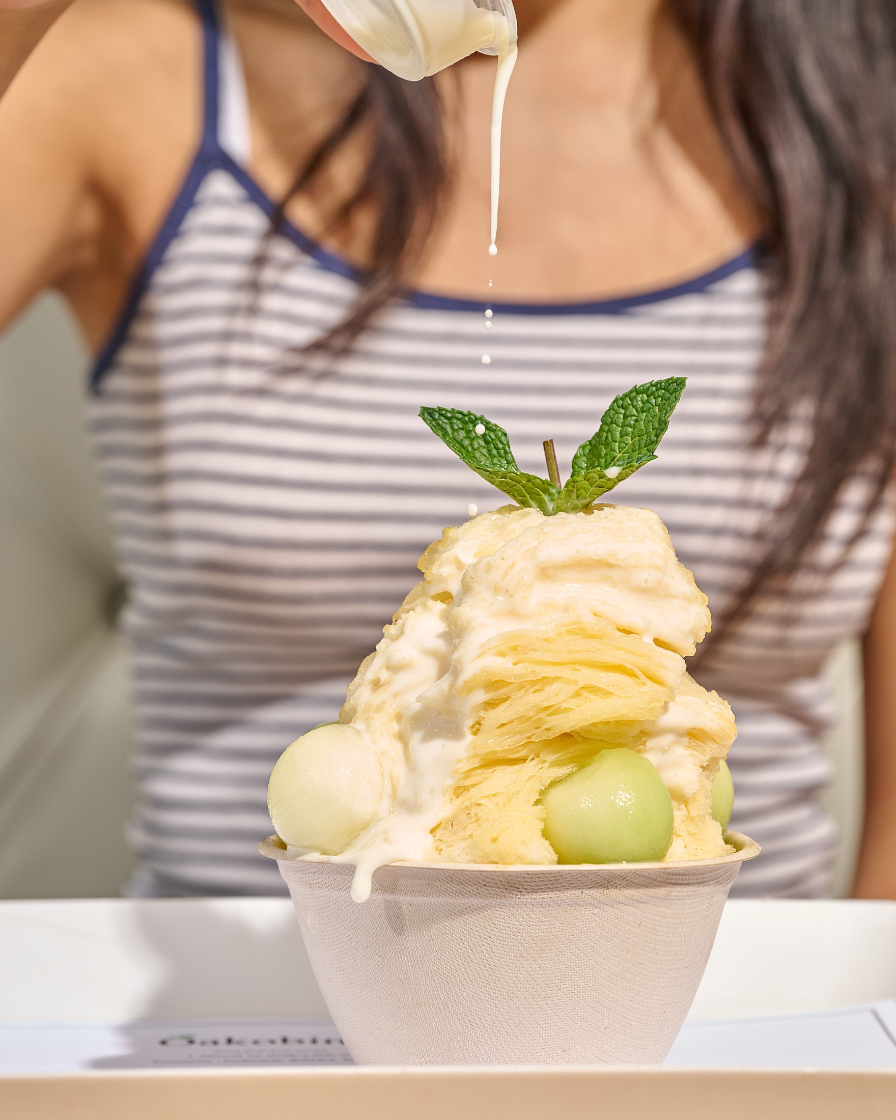 Milk drizzle poured over Oakobing signature mango melon bingsu with melon balls