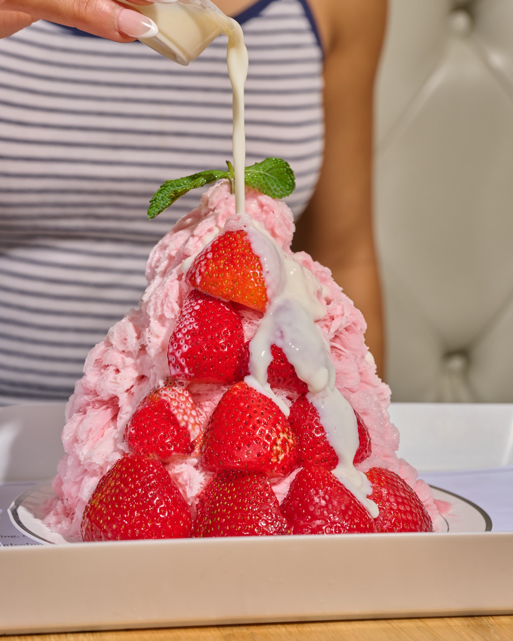 Milk drizzle poured over a tall strawberry bingsu, sweetness controlled at the table