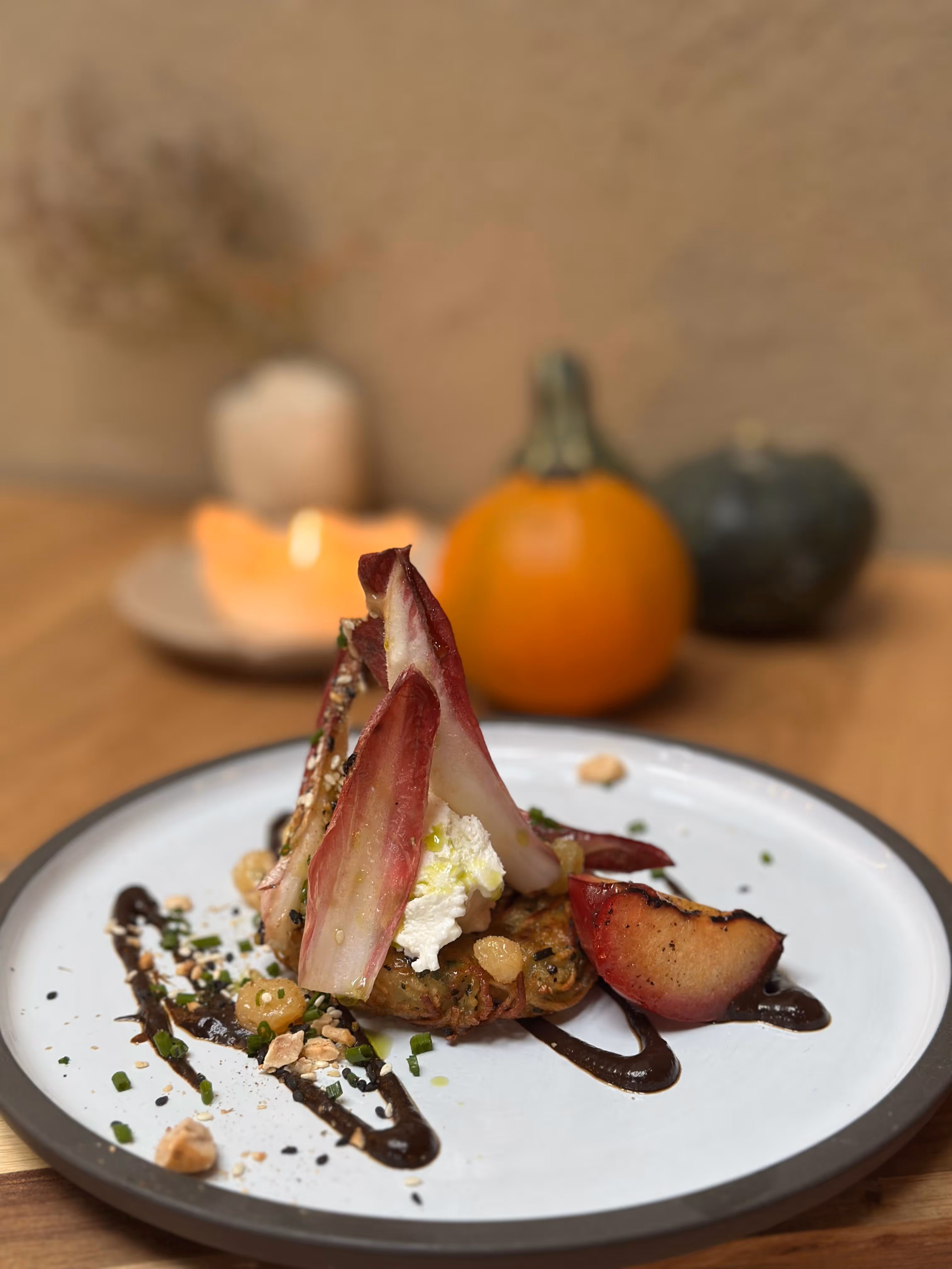 Gourmet dish with endive, creamy cheese, sauce, and nuts on white plate with pumpkins in background.