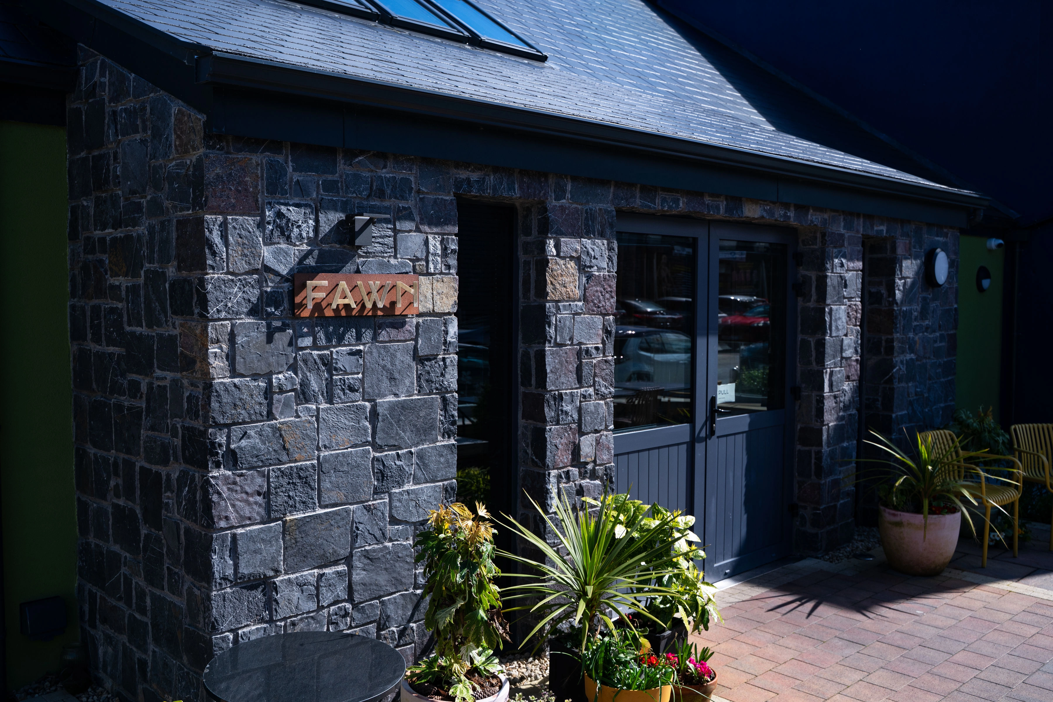 Stone building facade with a sign reading 'FAWN' and potted plants near double doors.