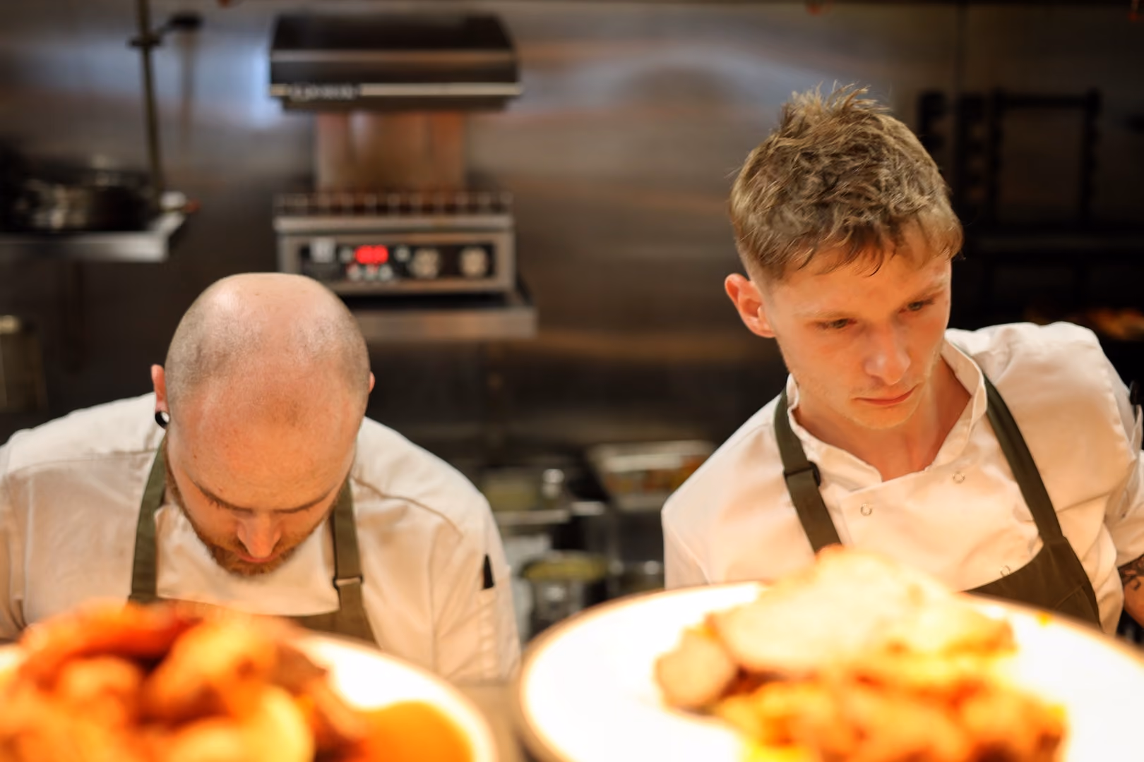Two chefs with aprons focused on preparing food in a professional kitchen.
