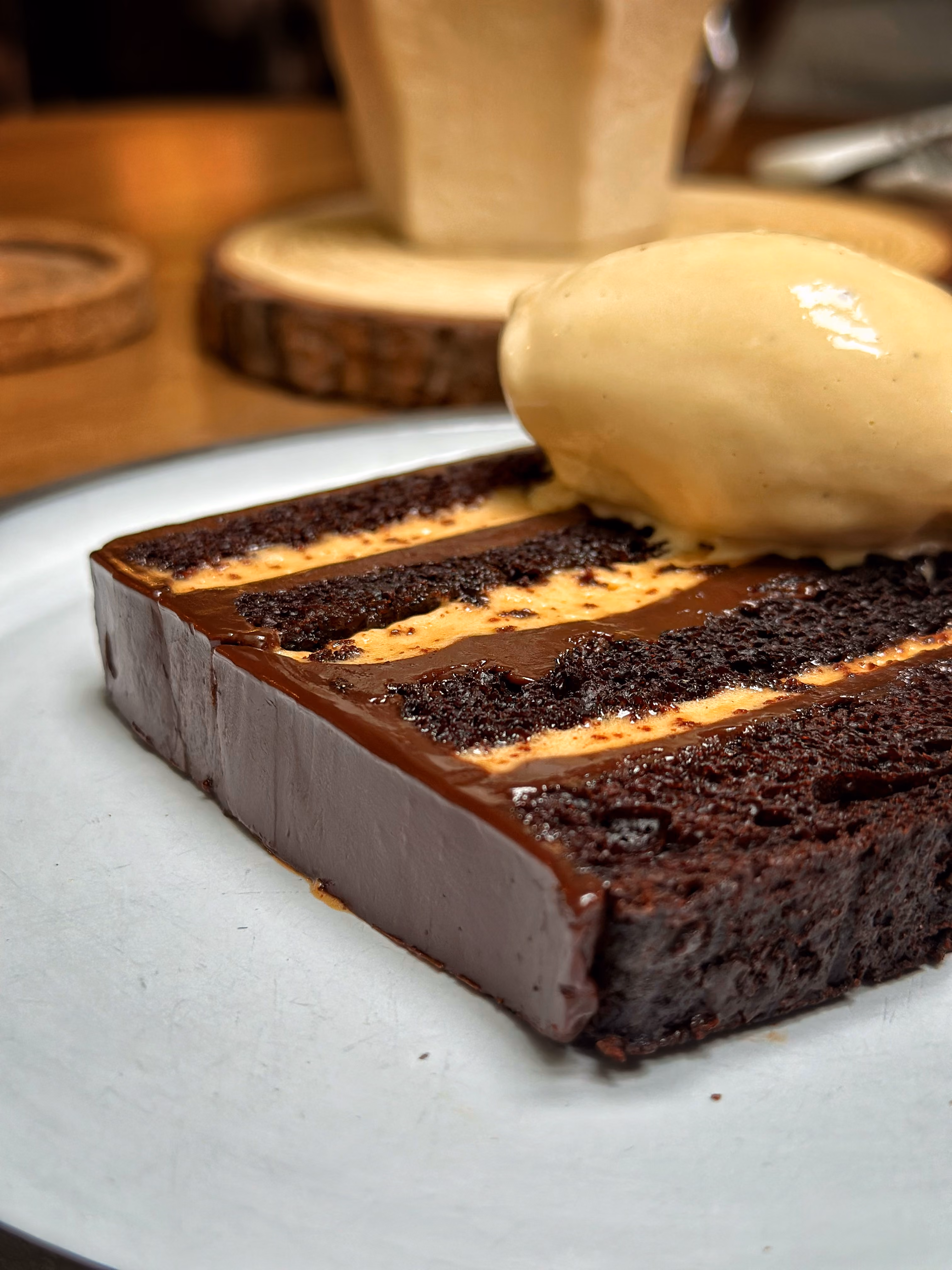 Slice of chocolate cake with creamy layers topped with a scoop of vanilla ice cream on a white plate.