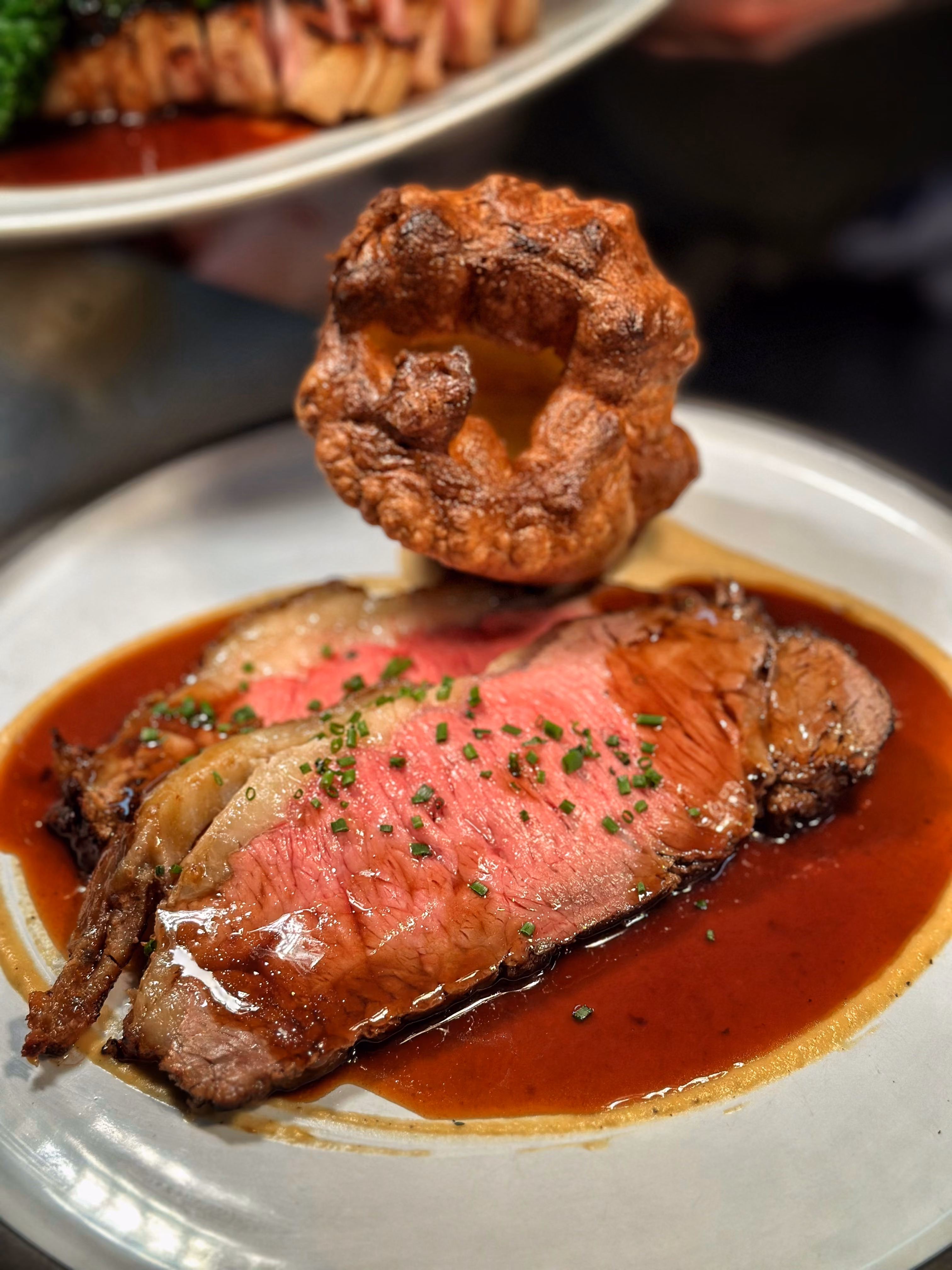 Two slices of medium rare roast beef with gravy and a crispy Yorkshire pudding on a white plate.