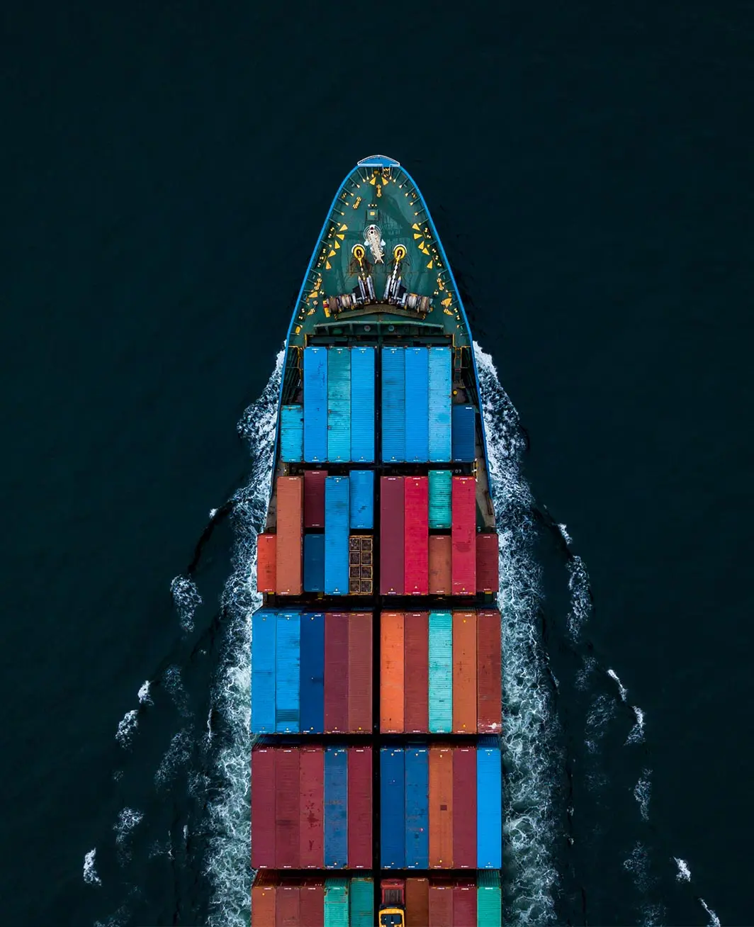Overhead view of a cargo ship with multicolored containers sailing through dark ocean water.