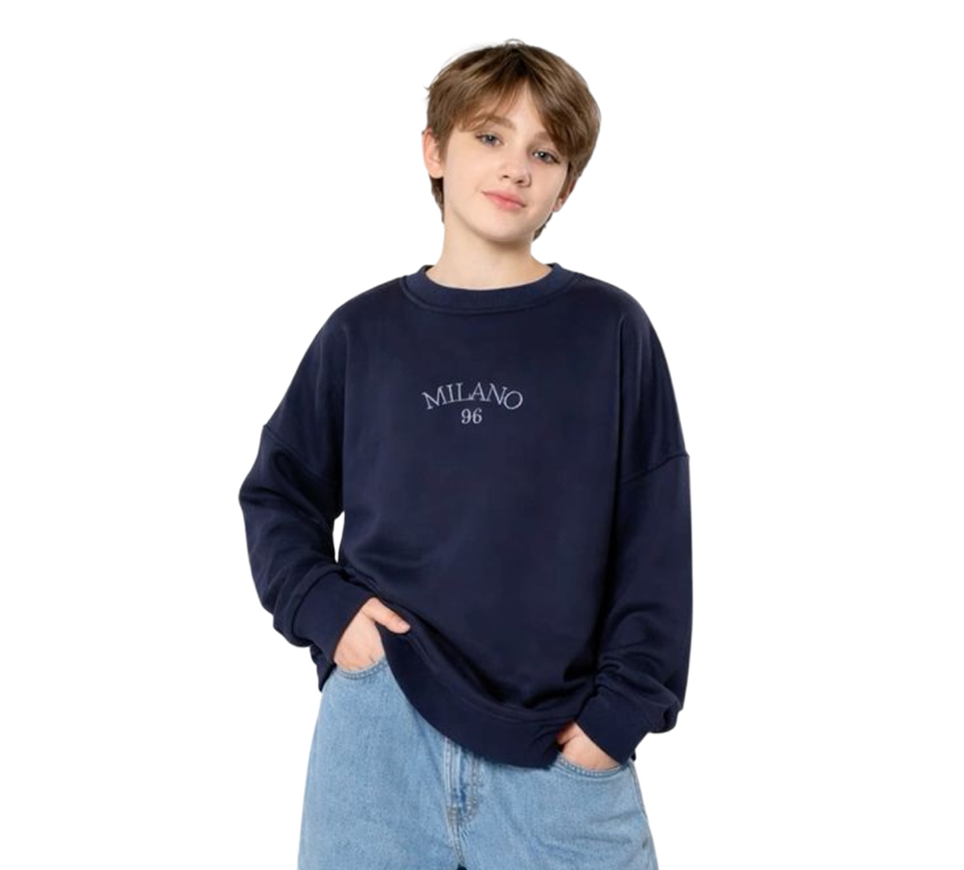 Young person wearing a navy sweatshirt with 'MILANO 96' printed on it and light blue jeans with hands in pockets.